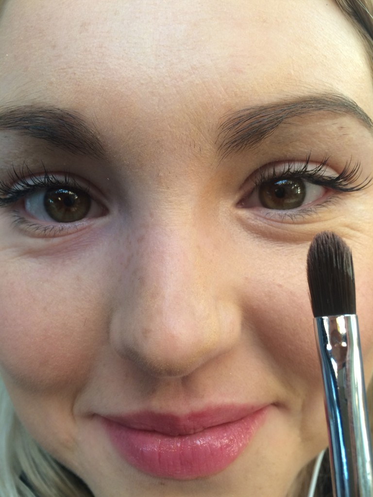 A girl using a concealer brush to blend the under-eye concealer